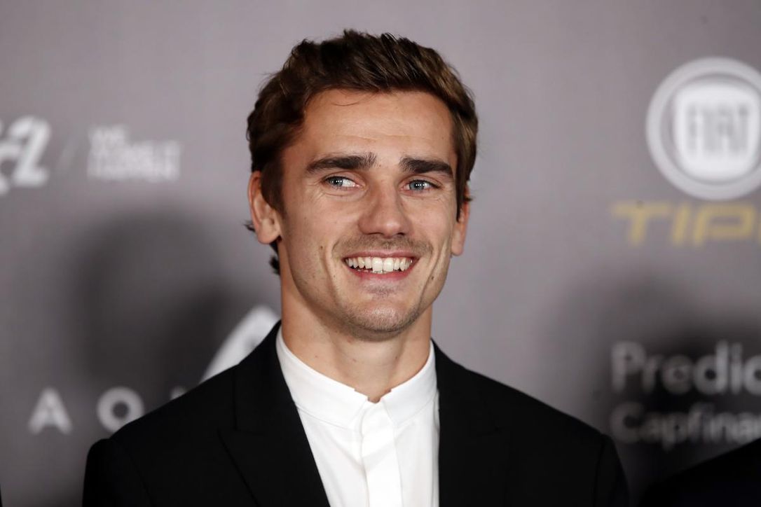 Antoine Griezmann wearing a black suit on a white shirt with a smile on his face at a football event